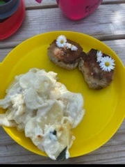 Billede af en tallerken med frikadeller pyntet med tusindfryd og en portion kartoffelsalat